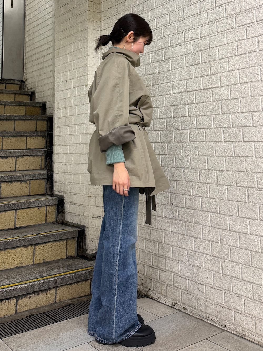 グリーン系のトレンチコート、グリーン系のニット/セーター、ブルー系のデニムパンツを着用したレディースの冬コーディネートの5枚目の写真