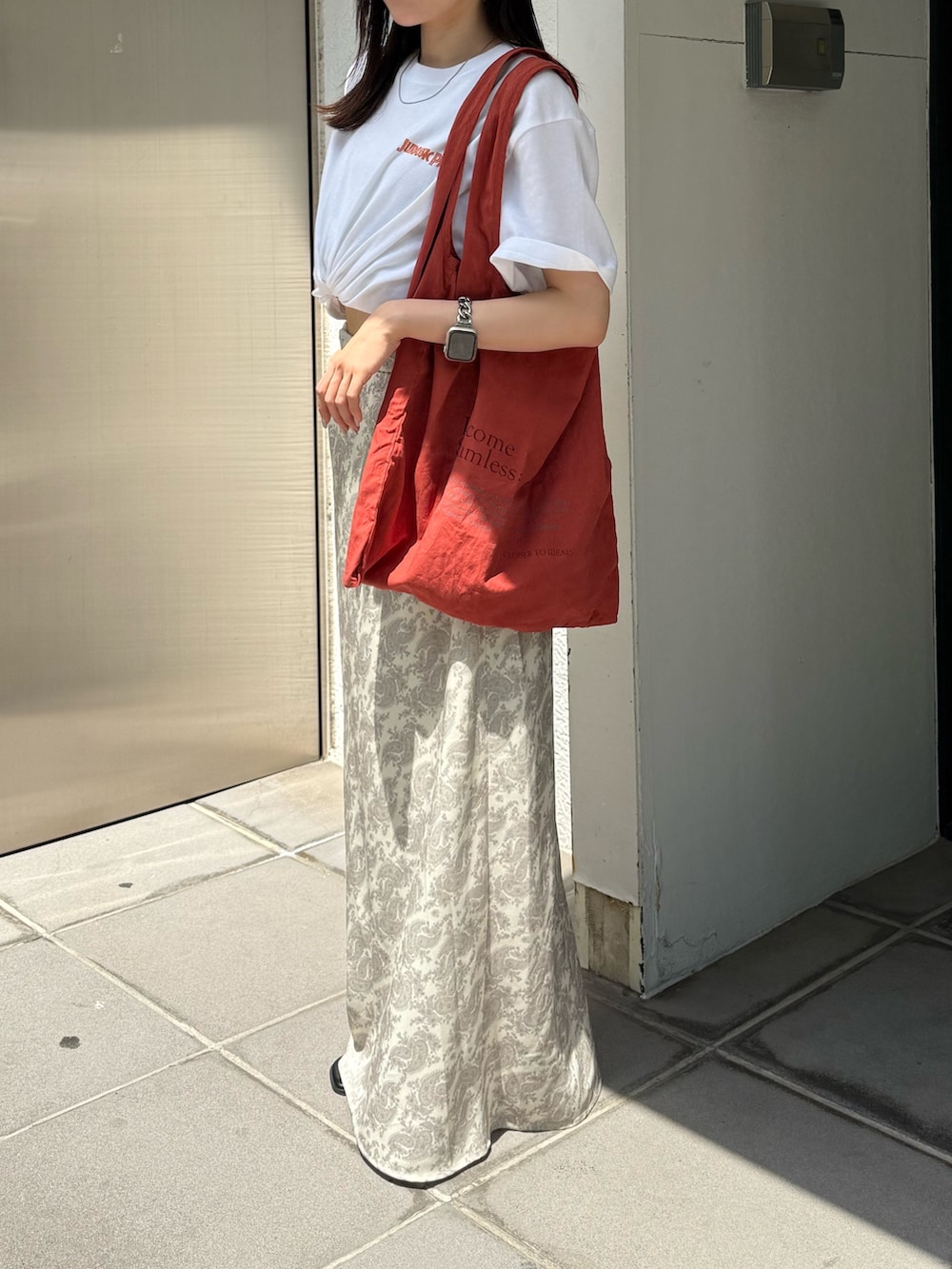オレンジ系のトートバッグ、ホワイト系のTシャツ/カットソー、ブラック系のサンダルを着用したレディースの夏コーディネートの2枚目の写真