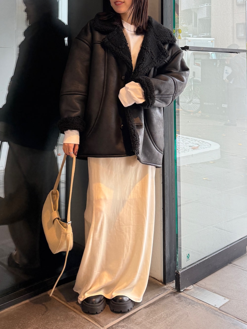 ブラック系のブルゾン、ベージュ系のハンドバッグ、ホワイト系のスカートを着用したレディースの冬コーディネートの7枚目の写真