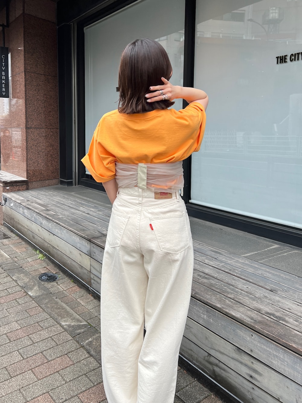 ホワイト系のデニムパンツ、ブラック系のサンダル、オレンジ系のTシャツ/カットソーを着用したレディースの春コーディネートの4枚目の写真