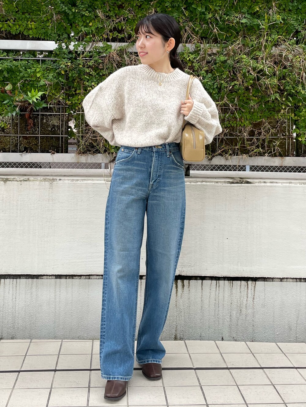 ブルー系のデニムパンツ、ブラウン系のブーツ、ベージュ系のハンドバッグを着用したレディースの秋コーディネートの5枚目の写真