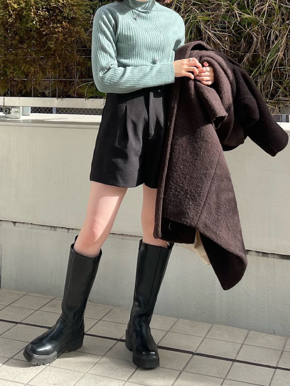 グリーン系のニット/セーター、ブラウン系のチェスターコート、ホワイト系のハンドバッグを着用したレディースの冬コーディネートの3枚目の写真