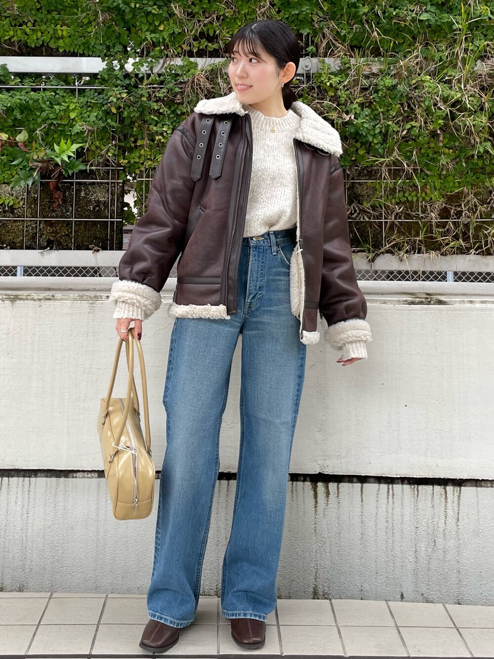 ブルー系のデニムパンツ、ブラウン系のブーツ、ベージュ系のハンドバッグを着用したレディースの秋コーディネートの2枚目の写真