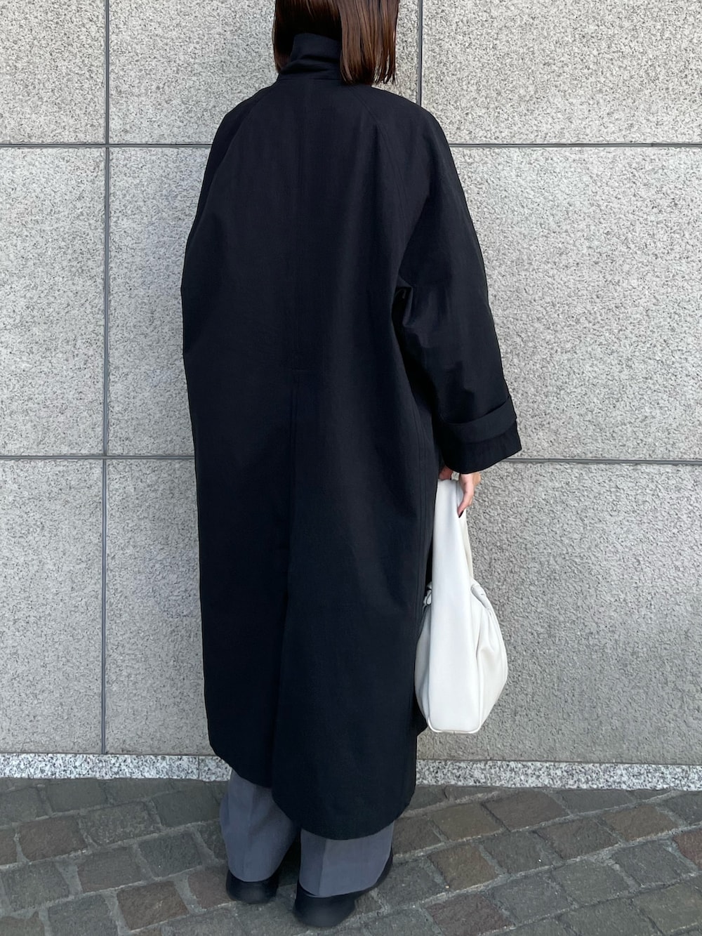 ホワイト系のハンドバッグ、ブラック系のステンカラーコート、グレー系のその他パンツを着用したレディースの春コーディネートの3枚目の写真