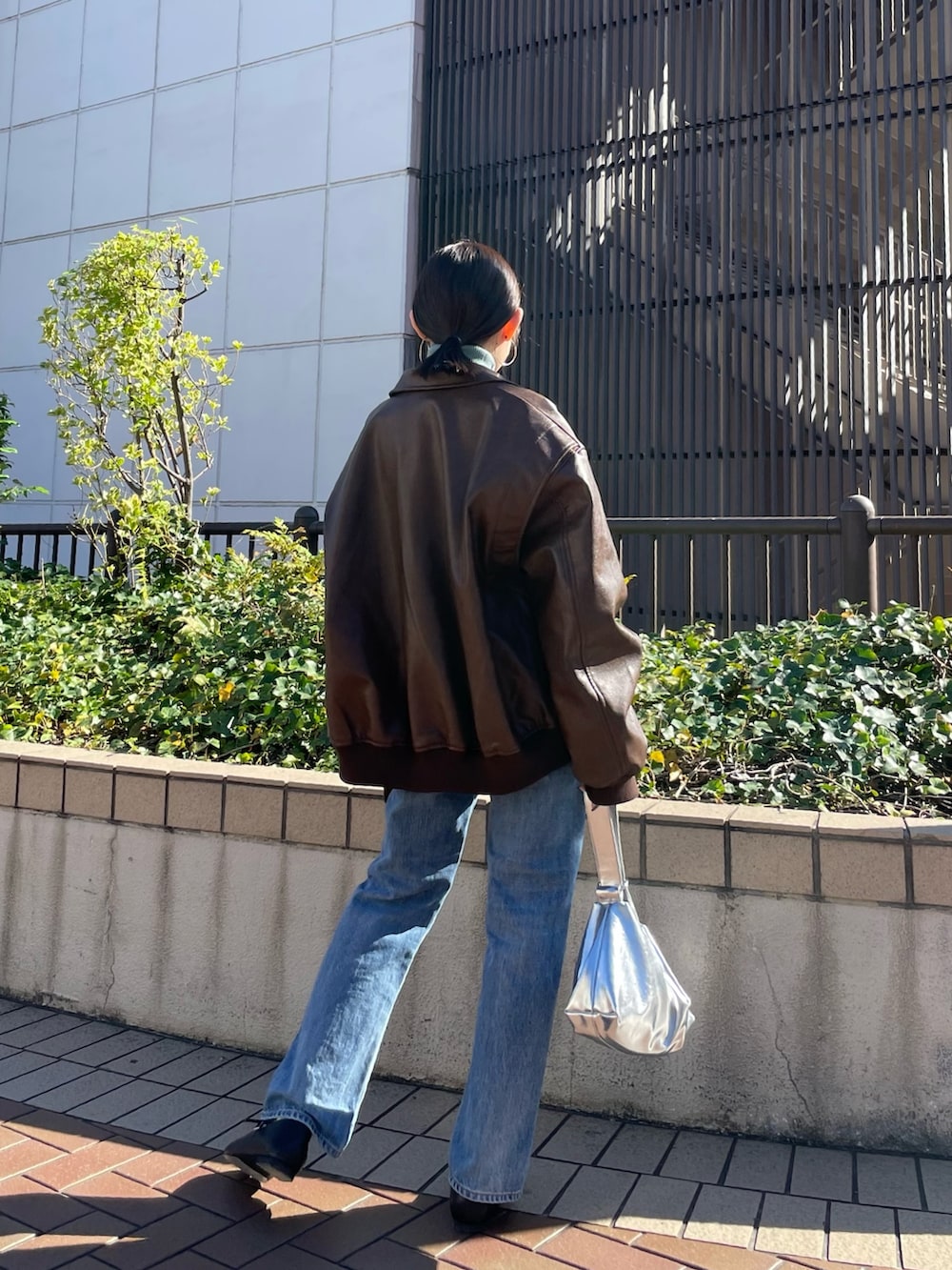 ブラウン系のブルゾン、ブラック系のパンプス、ブルー系のデニムパンツを着用したレディースの秋コーディネートの5枚目の写真