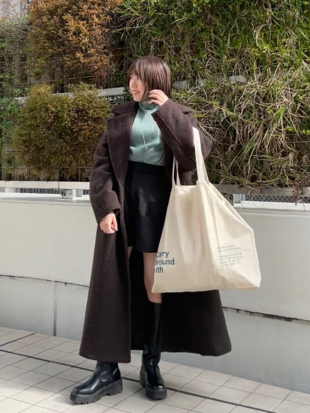 グリーン系のニット/セーター、ブラウン系のチェスターコート、ホワイト系のハンドバッグを着用したレディースの冬コーディネートの2枚目の写真