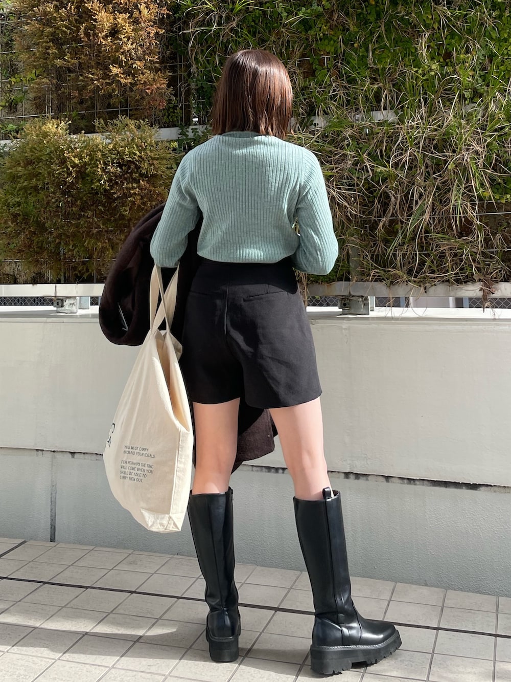 グリーン系のニット/セーター、ブラウン系のチェスターコート、ホワイト系のハンドバッグを着用したレディースの冬コーディネートの4枚目の写真