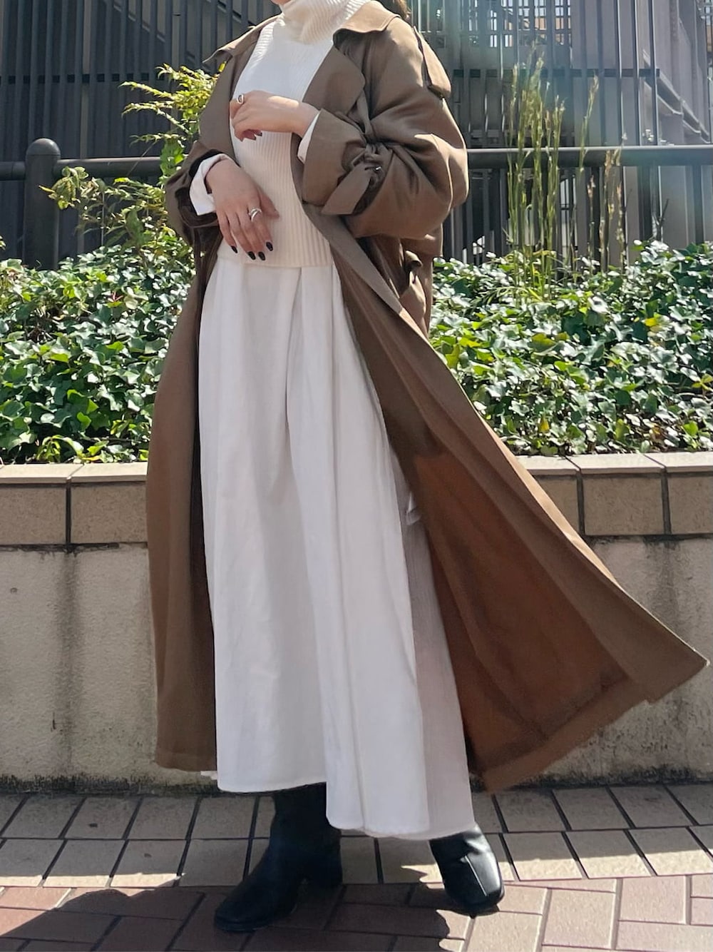 ブラウン系のトレンチコート、ブラック系のブーツ、ホワイト系のワンピースを着用したレディースの秋コーディネートの4枚目の写真