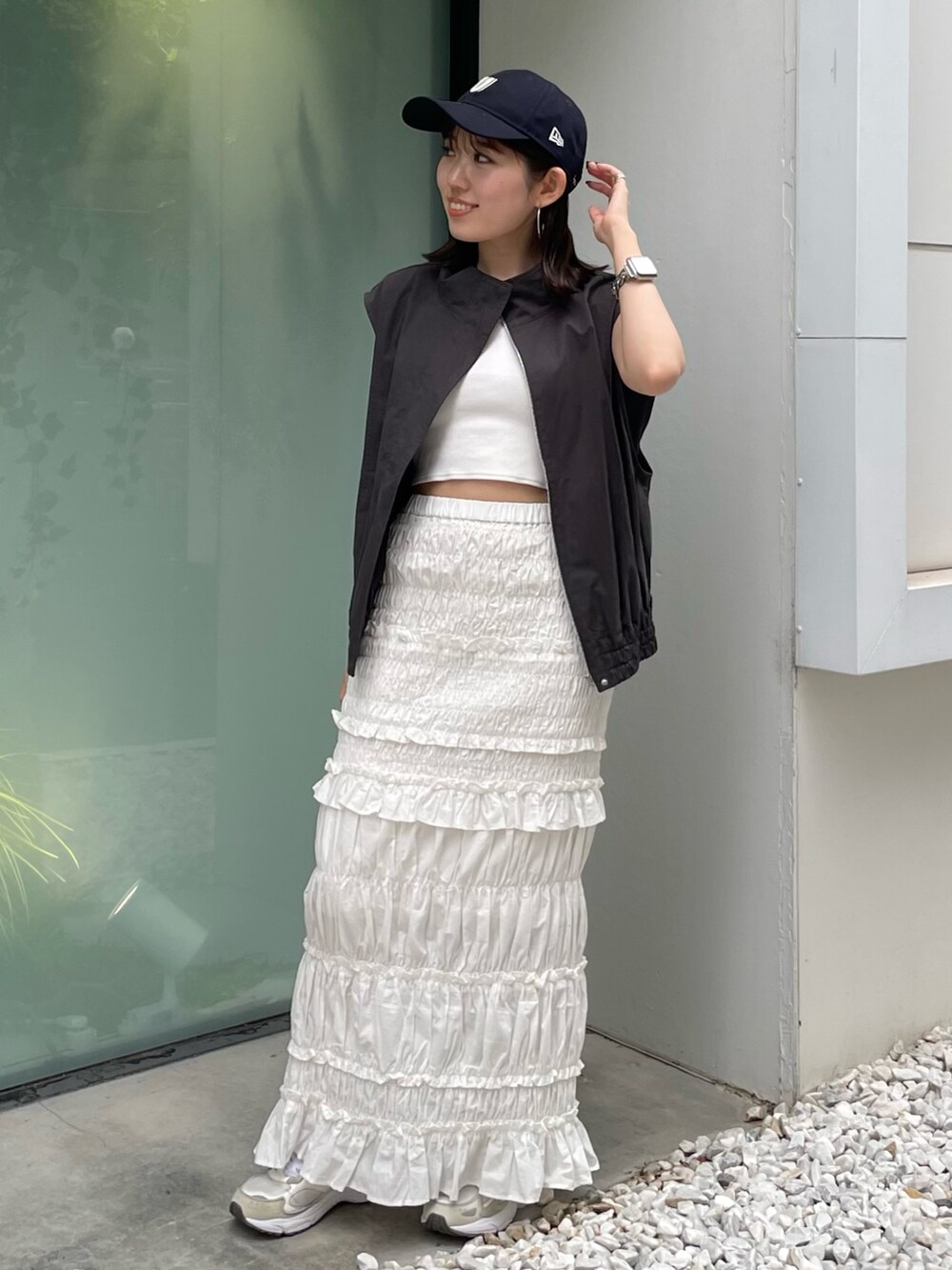 グレー系のベスト、ホワイト系のスカート、ブルー系のキャップを着用したレディースの夏コーディネートの2枚目の写真