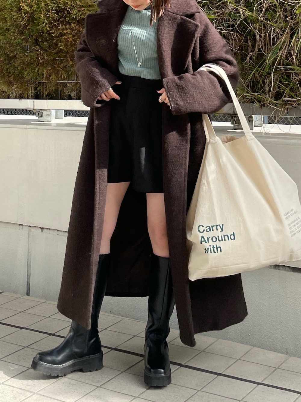 グリーン系のニット/セーター、ブラウン系のチェスターコート、ホワイト系のハンドバッグを着用したレディースの冬コーディネートの7枚目の写真