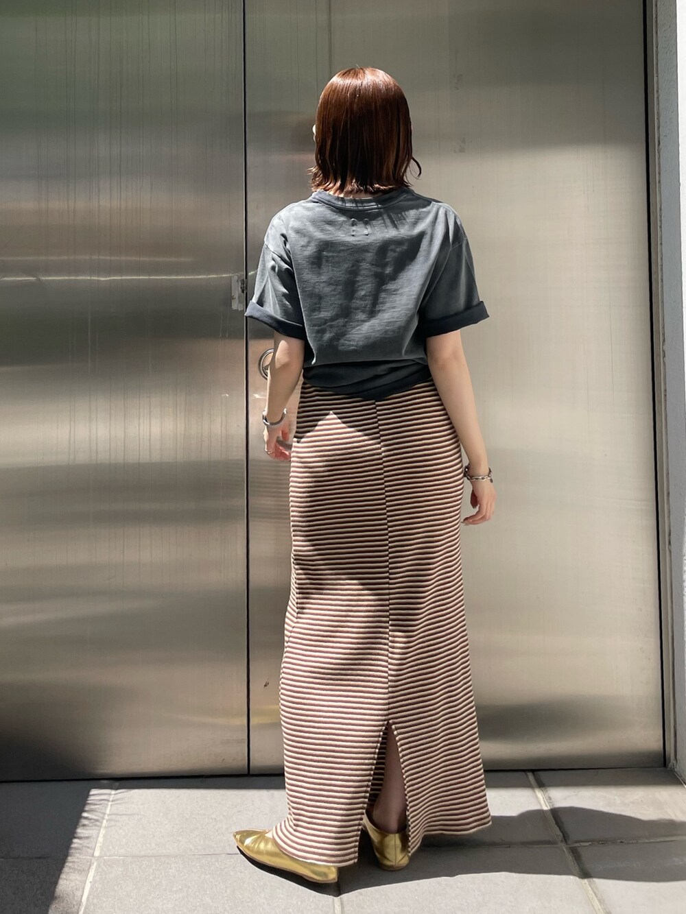 ブラウン系のワンピース、ゴールド系のパンプス、グレー系のTシャツ/カットソーを着用したレディースの夏コーディネートの4枚目の写真