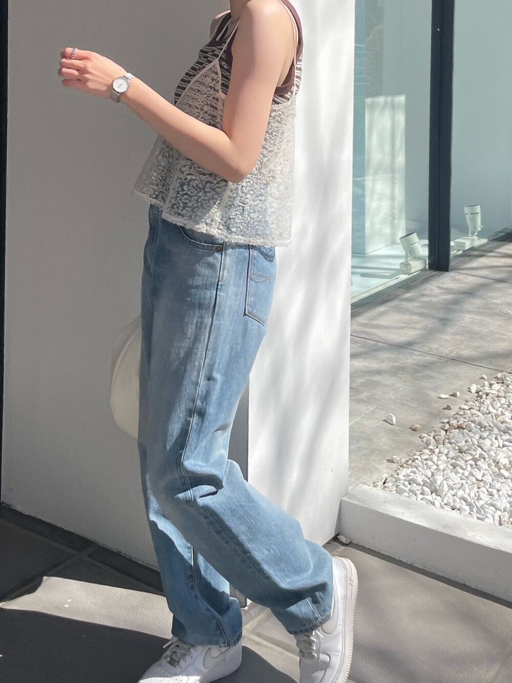 ホワイト系のハンドバッグ、ブルー系のデニムパンツ、ホワイト系のキャミソールを着用したレディースの春コーディネートの3枚目の写真