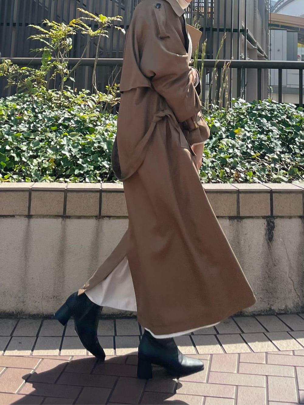 ブラウン系のトレンチコート、ブラック系のブーツ、ホワイト系のワンピースを着用したレディースの秋コーディネートの5枚目の写真