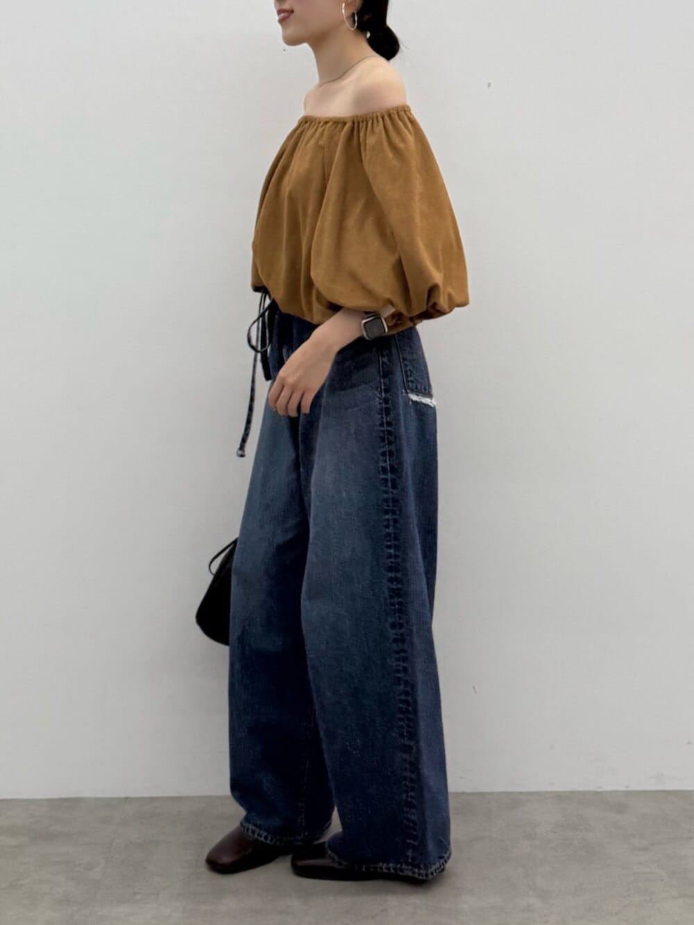 ブラウン系のブーツ、ブラック系のショルダーバッグ、ブルー系のデニムパンツを着用したレディースの秋コーディネートの2枚目の写真