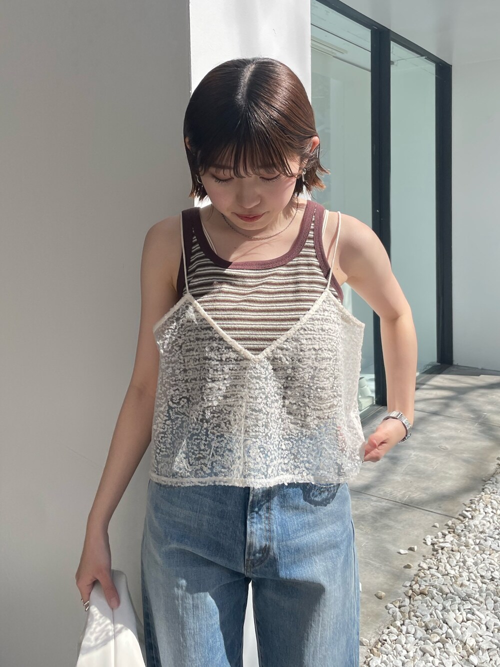 ホワイト系のハンドバッグ、ブルー系のデニムパンツ、ホワイト系のキャミソールを着用したレディースの春コーディネートの4枚目の写真