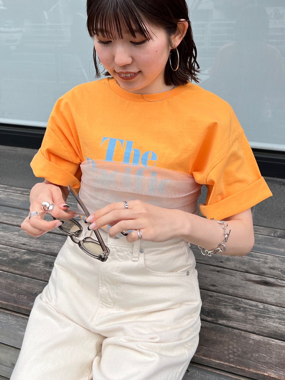 ホワイト系のデニムパンツ、ブラック系のサンダル、オレンジ系のTシャツ/カットソーを着用したレディースの春コーディネートの7枚目の写真