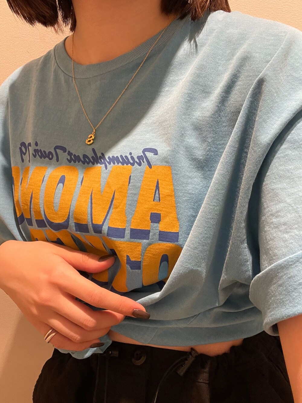 ブルー系のTシャツ/カットソー、ブラック系のスカート、ゴールド系のネックレスを着用したレディースの春コーディネートの5枚目の写真