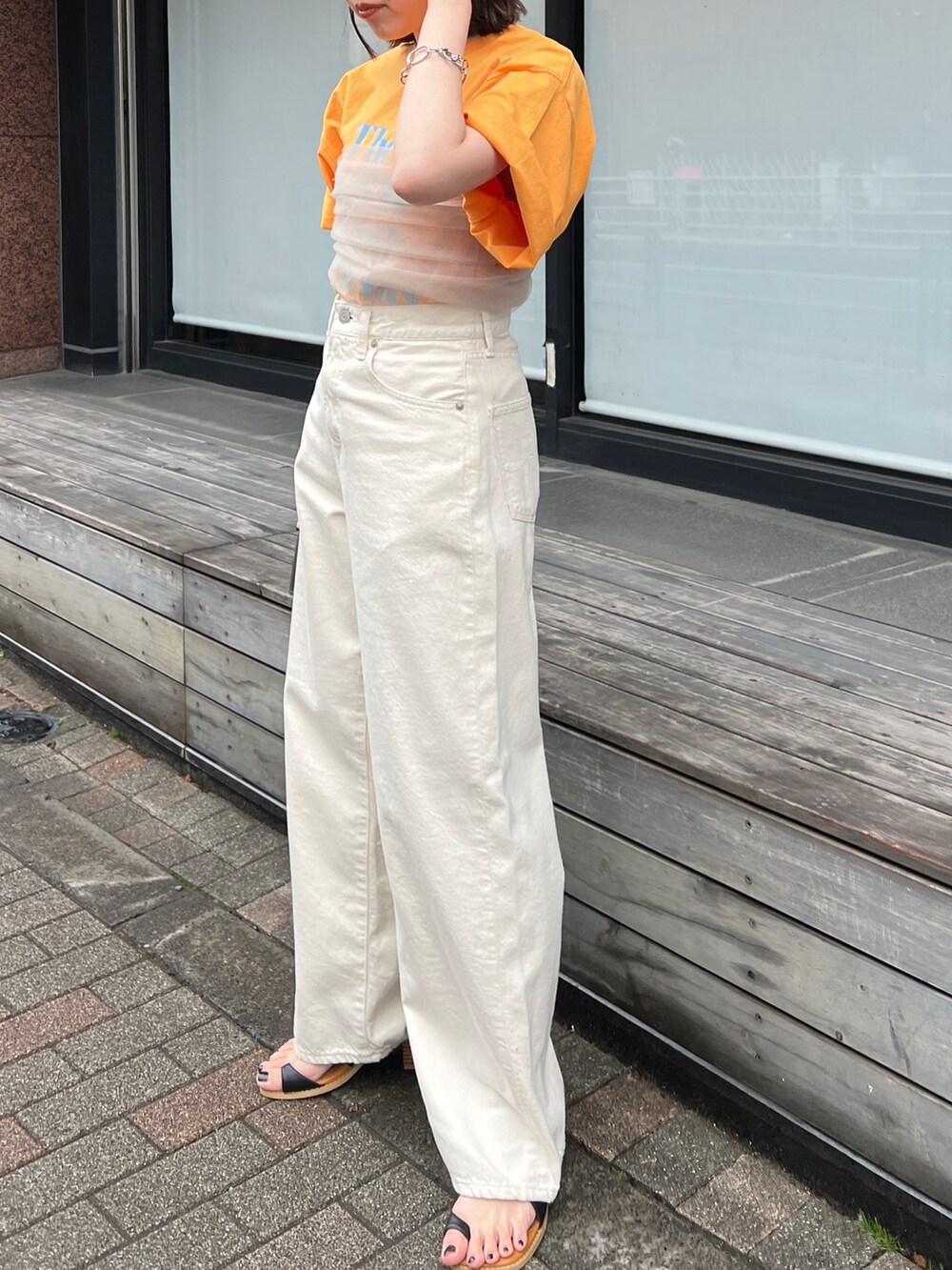 ホワイト系のデニムパンツ、ブラック系のサンダル、オレンジ系のTシャツ/カットソーを着用したレディースの春コーディネートの5枚目の写真