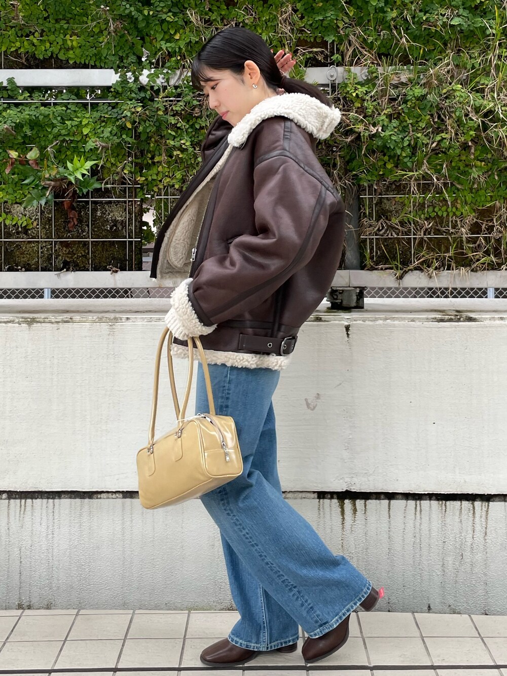 ブルー系のデニムパンツ、ブラウン系のブーツ、ベージュ系のハンドバッグを着用したレディースの秋コーディネートの3枚目の写真