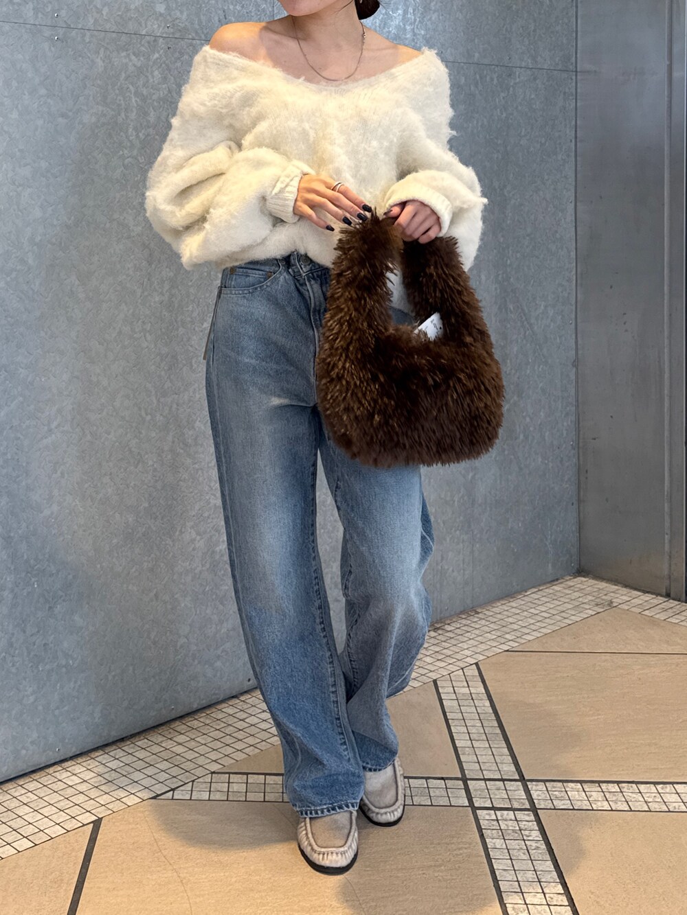 ブルー系のデニムパンツ、ブラウン系のハンドバッグ、ホワイト系のニット/セーターを着用したレディースの秋コーディネートの5枚目の写真