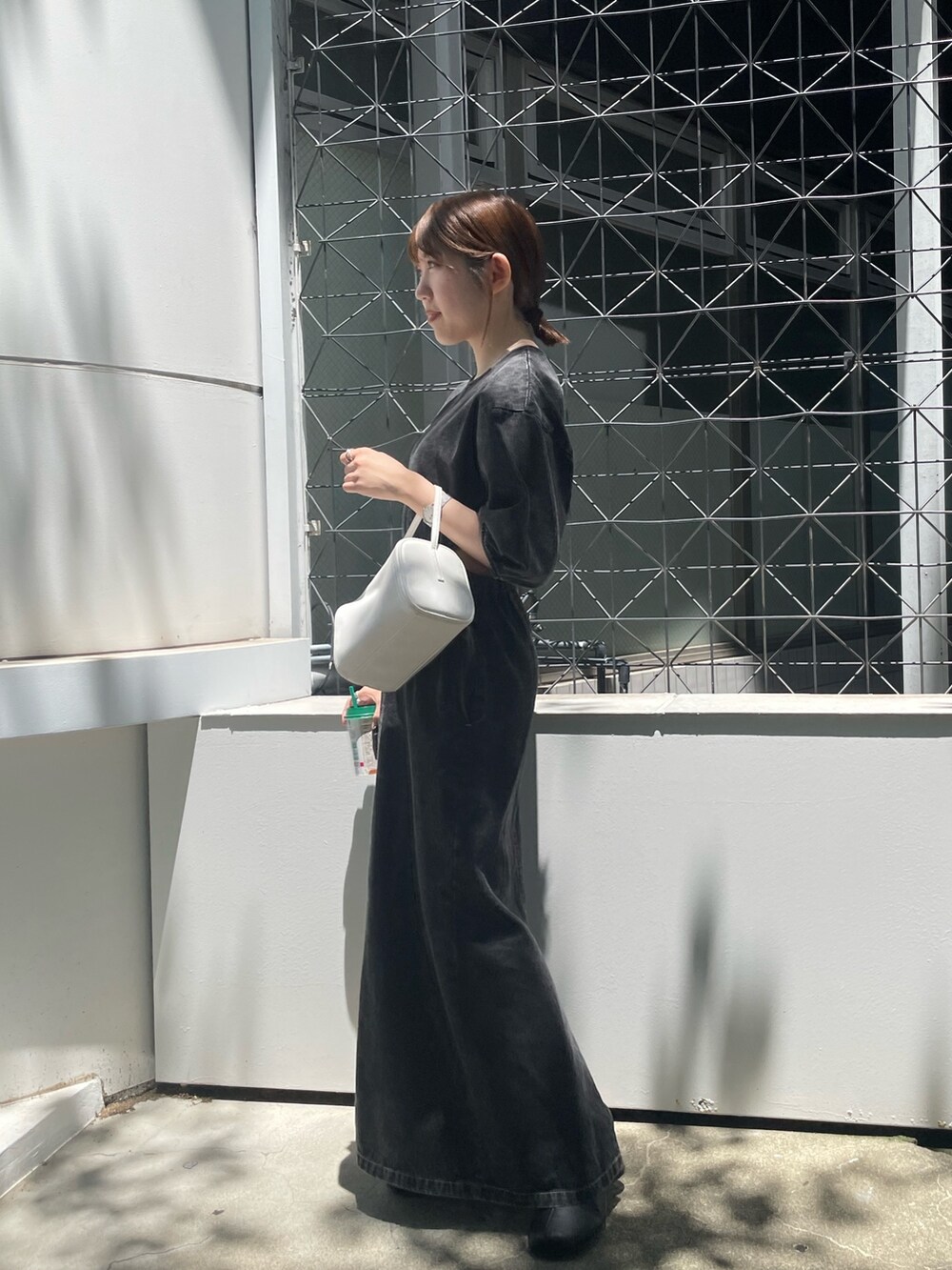 ホワイト系のハンドバッグ、ブラック系のブーツ、ブラック系のワンピースを着用したレディースの夏コーディネートの2枚目の写真