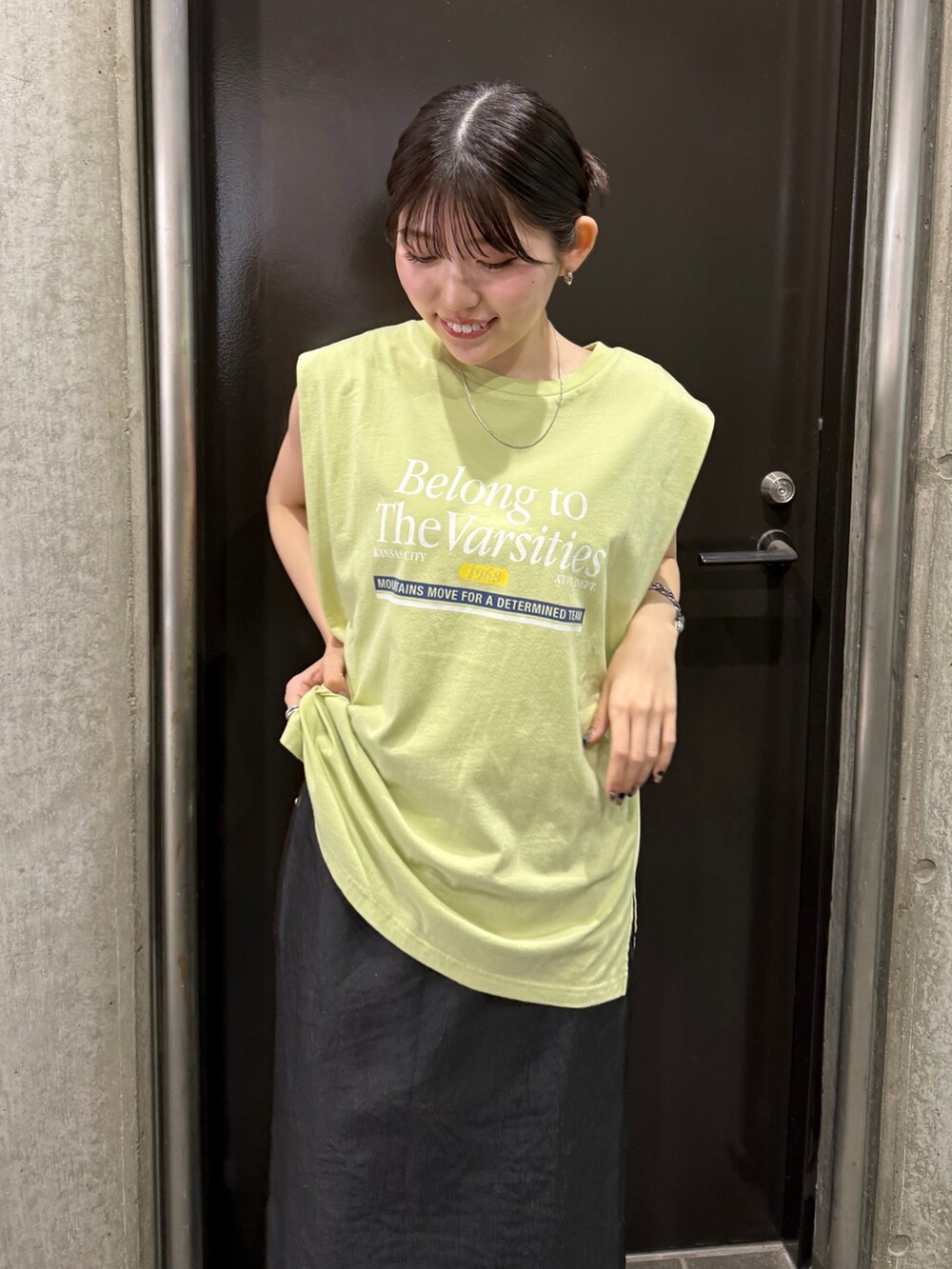 グレー系のスカート、グリーン系のタンクトップ、ブラック系のサンダルを着用したレディースの夏コーディネートの2枚目の写真