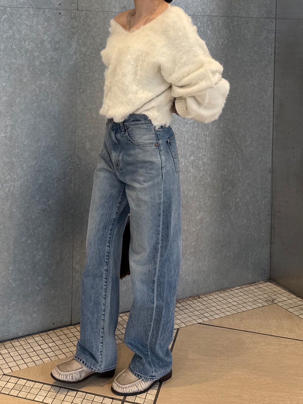 ブルー系のデニムパンツ、ブラウン系のハンドバッグ、ホワイト系のニット/セーターを着用したレディースの秋コーディネートの4枚目の写真