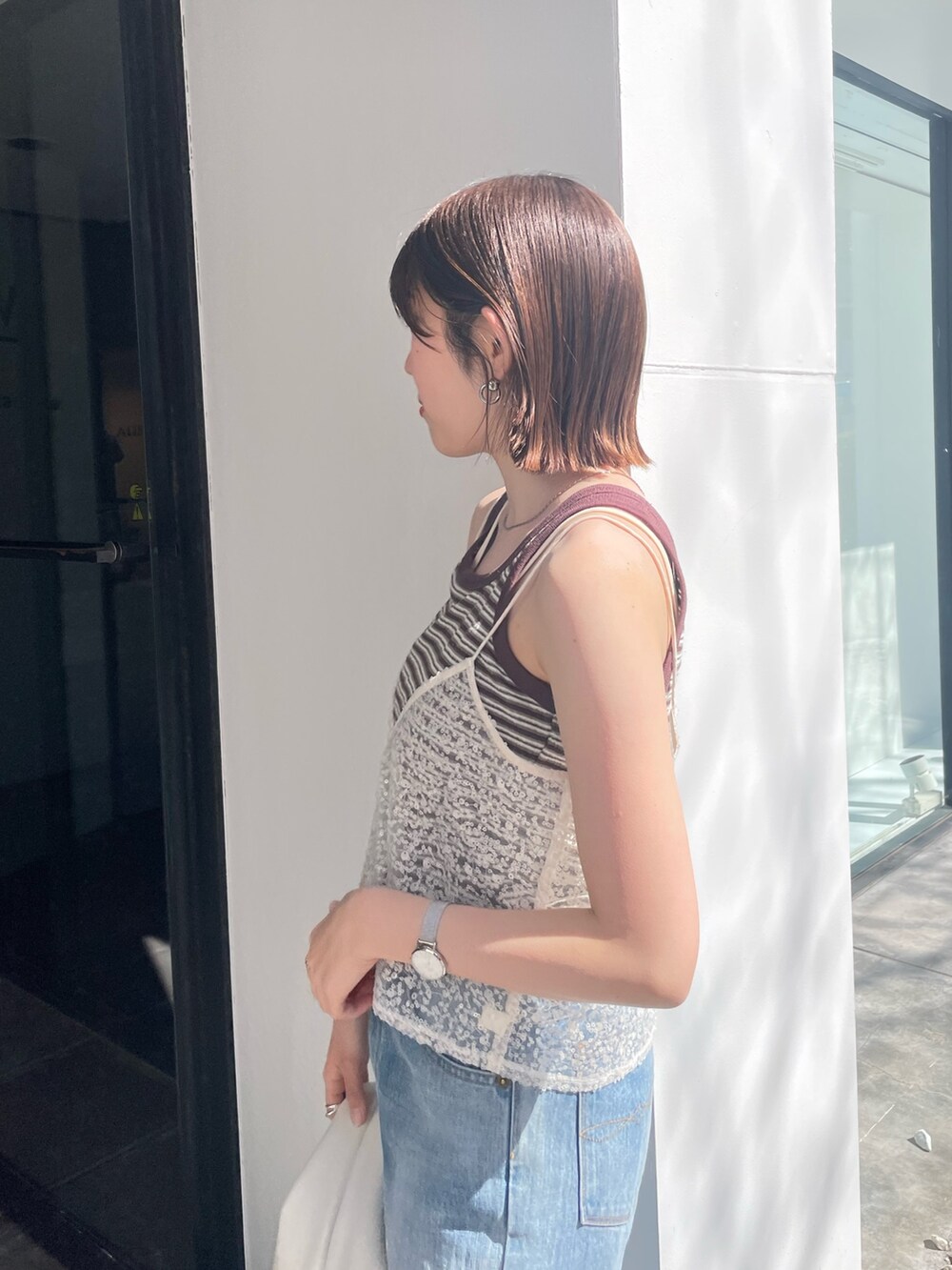 ホワイト系のハンドバッグ、ブルー系のデニムパンツ、ホワイト系のキャミソールを着用したレディースの春コーディネートの7枚目の写真