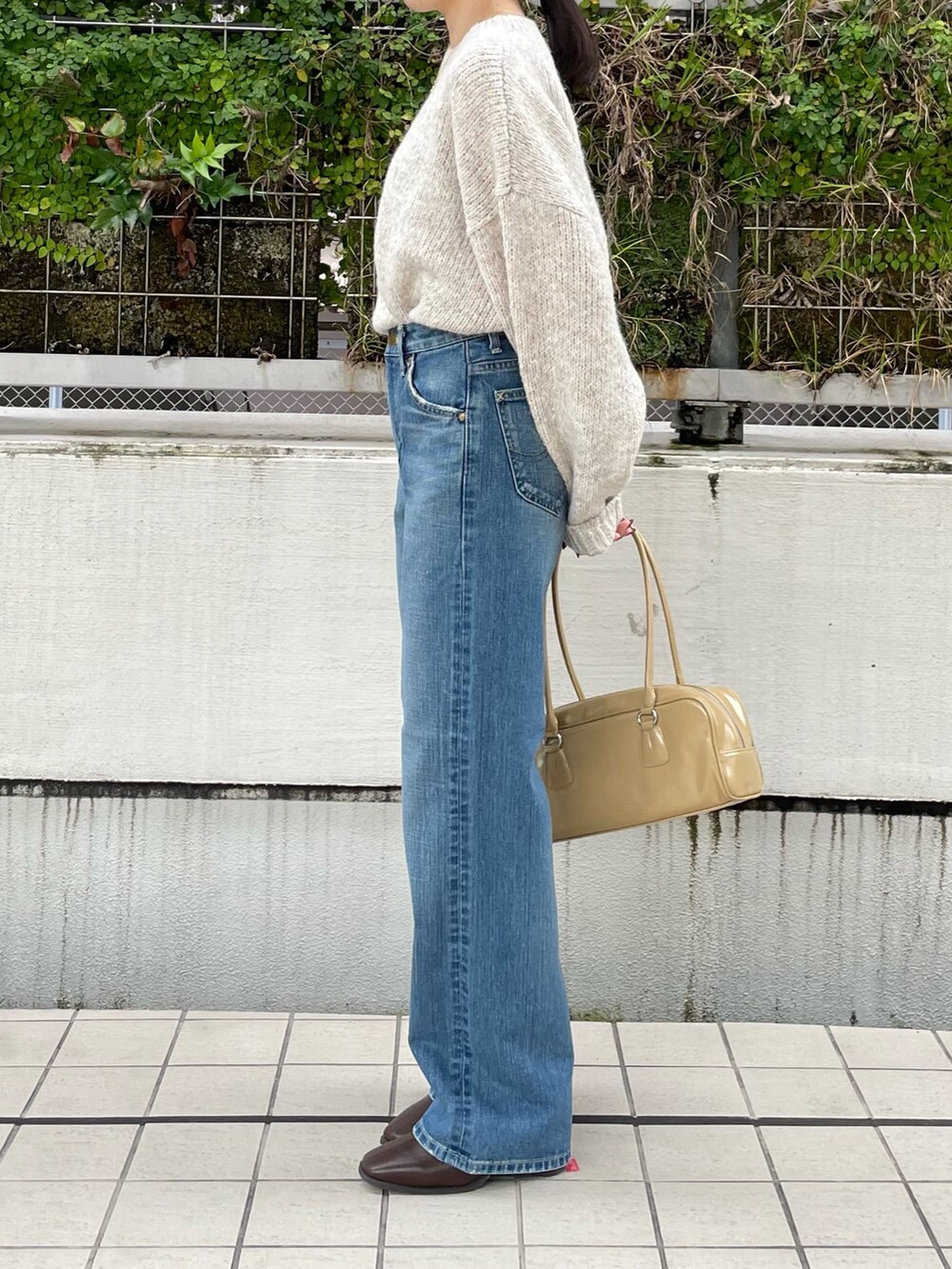 ブルー系のデニムパンツ、ブラウン系のブーツ、ベージュ系のハンドバッグを着用したレディースの秋コーディネートの6枚目の写真