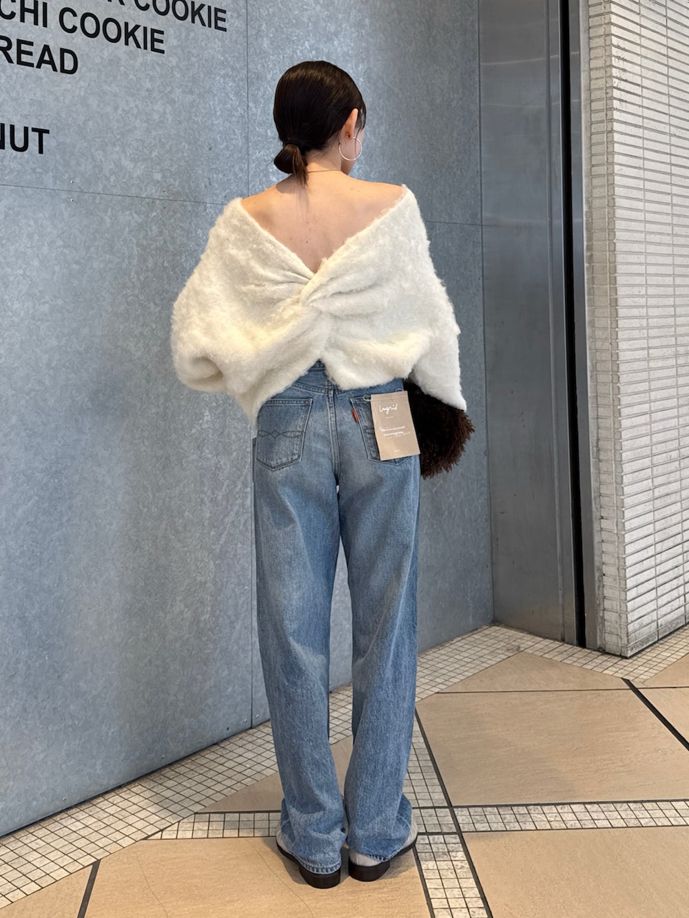 ブルー系のデニムパンツ、ブラウン系のハンドバッグ、ホワイト系のニット/セーターを着用したレディースの秋コーディネートの2枚目の写真