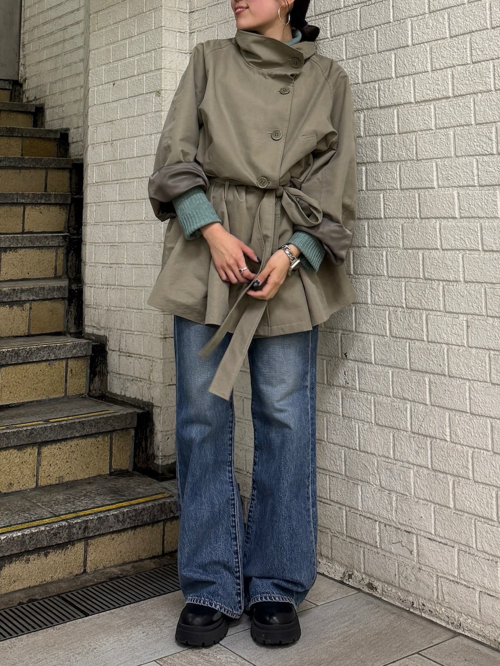 グリーン系のトレンチコート、グリーン系のニット/セーター、ブルー系のデニムパンツを着用したレディースの冬コーディネートの2枚目の写真