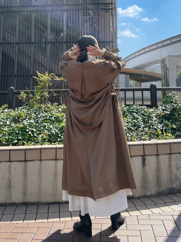 ブラウン系のトレンチコート、ブラック系のブーツ、ホワイト系のワンピースを着用したレディースの秋コーディネートの3枚目の写真