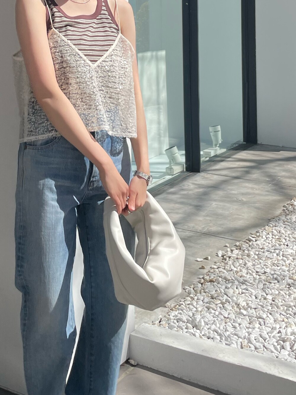 ホワイト系のハンドバッグ、ブルー系のデニムパンツ、ホワイト系のキャミソールを着用したレディースの春コーディネートの8枚目の写真