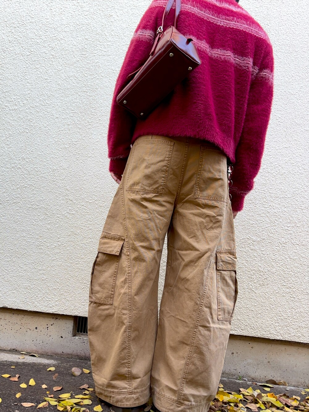 レッド系のニット/セーター、ベージュ系のチノパンツを着用したメンズの秋コーディネートの2枚目の写真