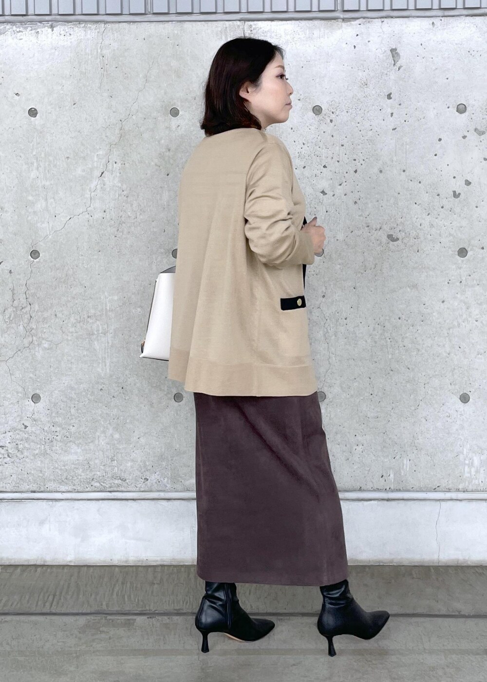 ベージュ系のニット/セーター、ブラウン系のスカート、ホワイト系のハンドバッグを着用したレディースの秋コーディネートの5枚目の写真