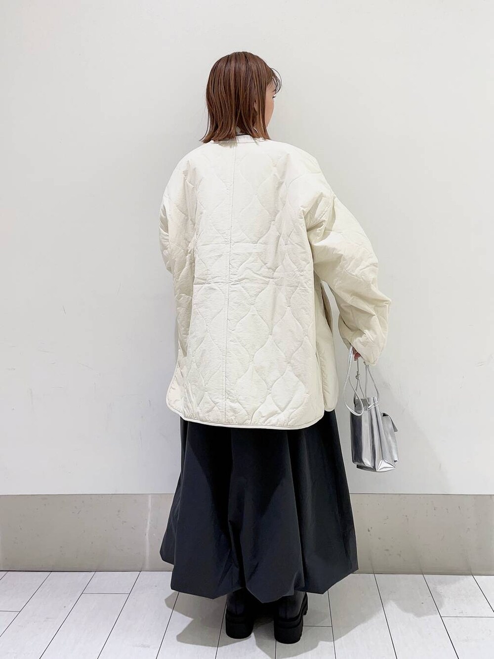 シルバー系のショルダーバッグ、ホワイト系のブルゾン、ブラック系のブーツを着用したレディースの秋コーディネートの2枚目の写真