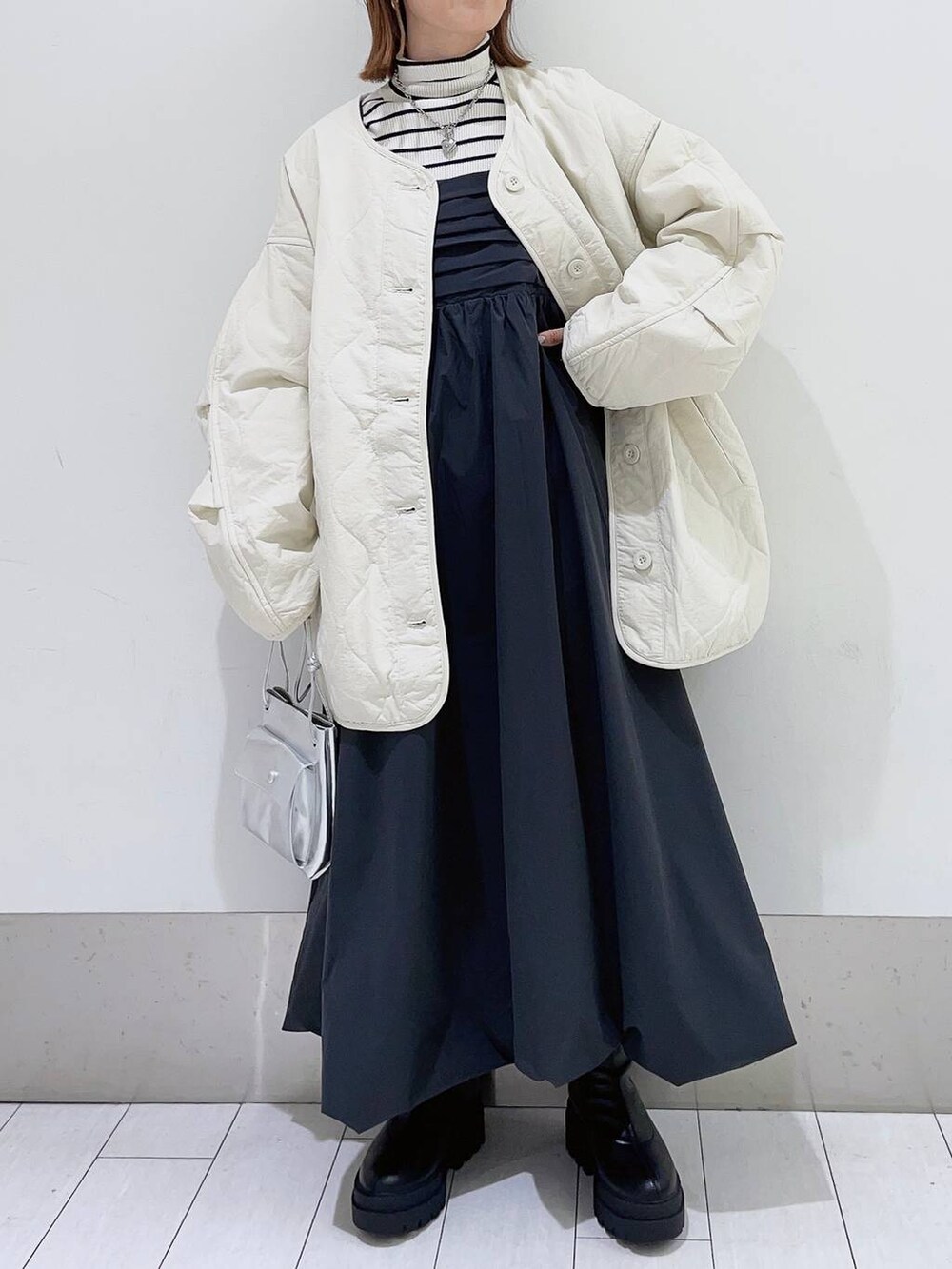 シルバー系のショルダーバッグ、ホワイト系のブルゾン、ブラック系のブーツを着用したレディースの秋コーディネートの3枚目の写真