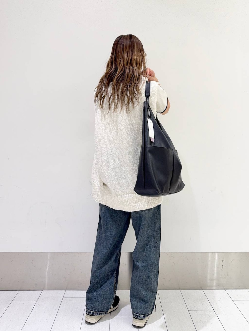 ブルー系のデニムパンツ、ブラック系のトートバッグ、ホワイト系のニット/セーターを着用したレディースの春コーディネートの3枚目の写真