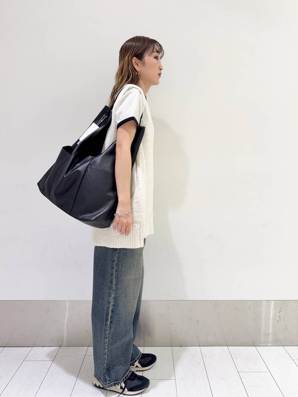 ブルー系のデニムパンツ、ブラック系のトートバッグ、ホワイト系のニット/セーターを着用したレディースの春コーディネートの2枚目の写真