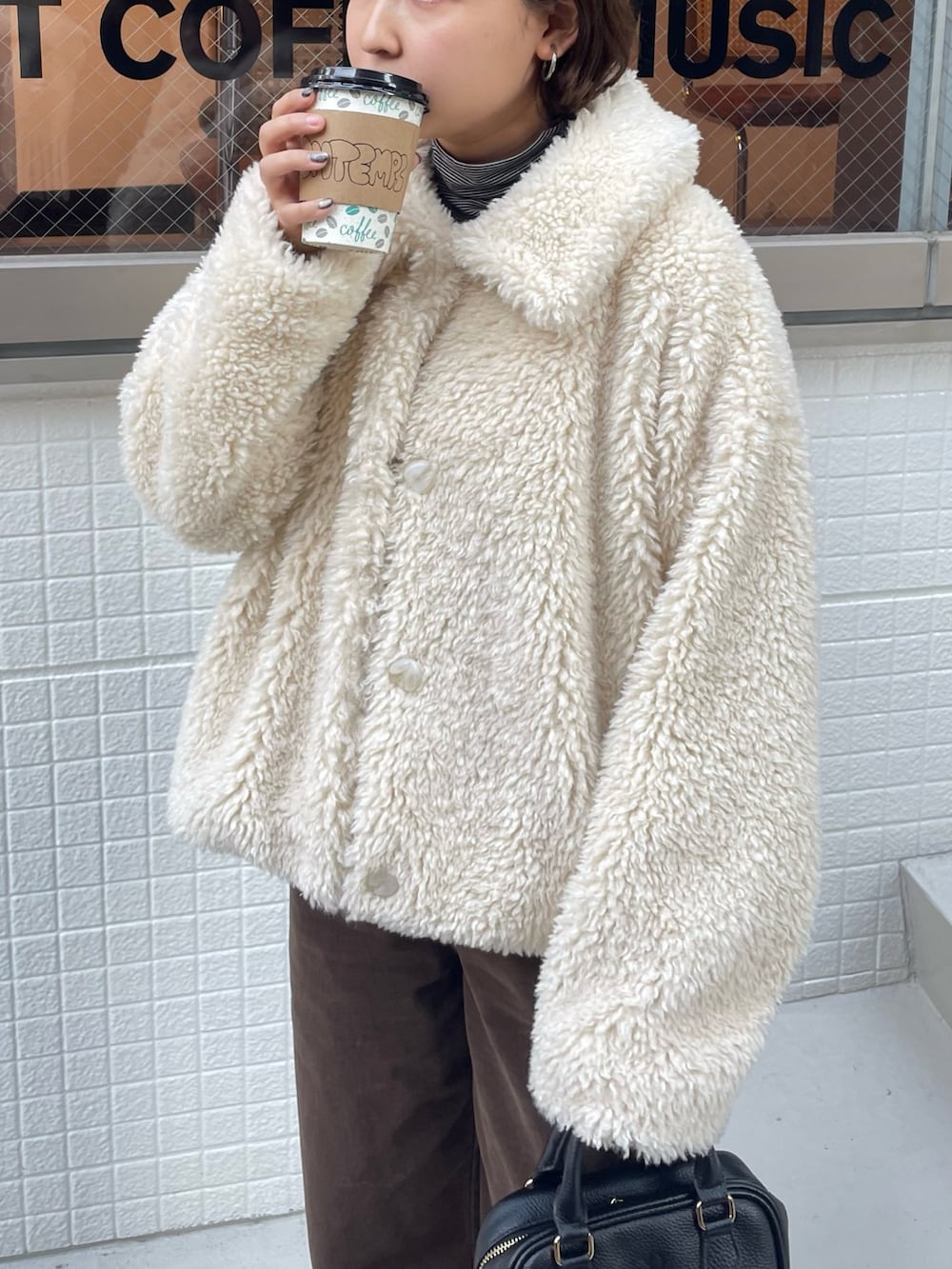 ホワイト系のムートンコート、ブラウン系のその他パンツ、ブラック系のショルダーバッグを着用したレディースの秋コーディネートの2枚目の写真