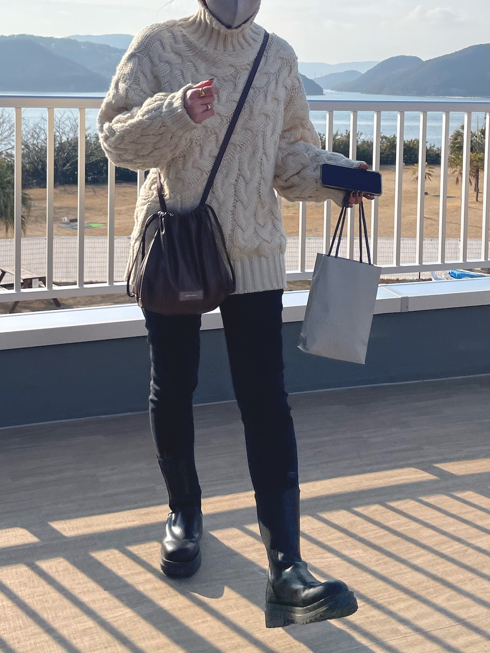 ブラウン系のショルダーバッグ、ブラック系のデニムパンツ、ブラック系のブーツを着用したレディースの冬コーディネートの2枚目の写真