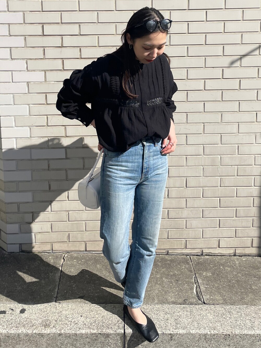 ブルー系のデニムパンツ、ホワイト系のハンドバッグ、ブラック系のシャツ/ブラウスを着用したレディースの冬コーディネートの2枚目の写真