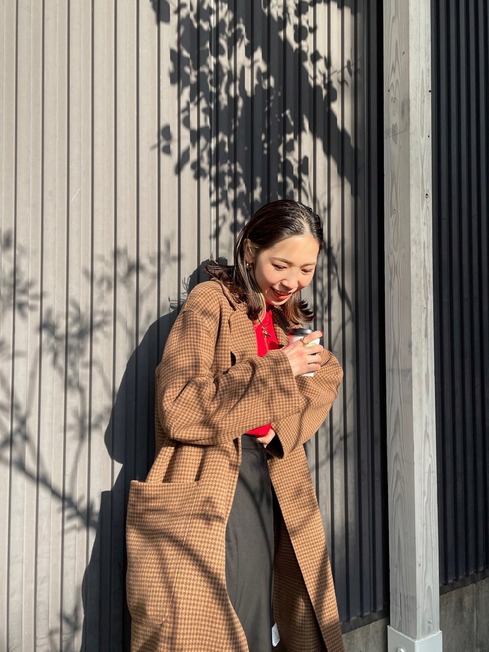 レッド系のニット/セーター、ブラウン系のチェスターコート、ブラック系のスカートを着用したレディースの冬コーディネートの2枚目の写真