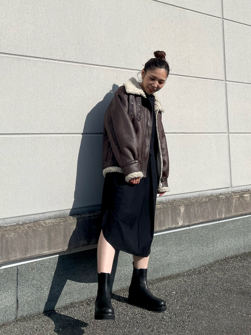 ブラウン系のブルゾン、ブラック系のブーツ、ブラック系のワンピースを着用したレディースの秋コーディネートの2枚目の写真