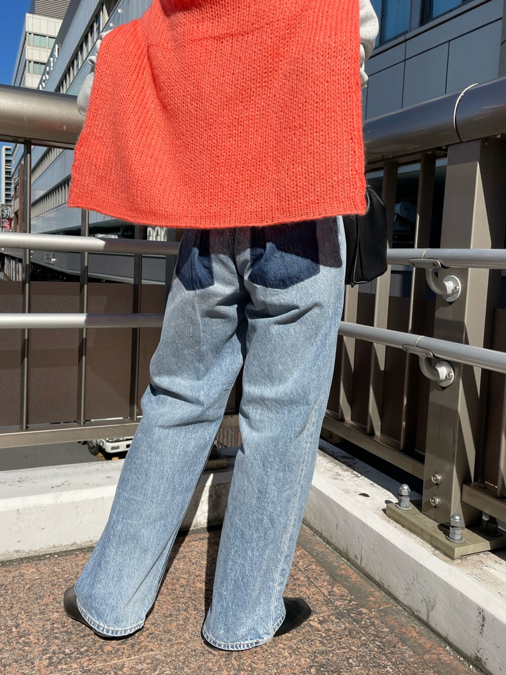 ブラック系のハンドバッグ、オレンジ系のニット/セーター、ブルー系のデニムパンツを着用したレディースの秋コーディネートの5枚目の写真