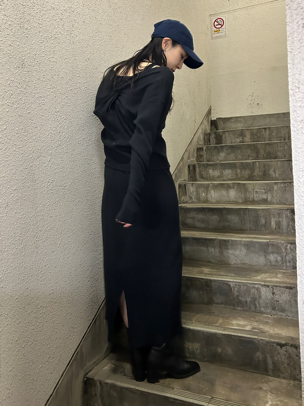 ブラック系のワンピース、ブラック系のブーツ、ブルー系のキャップを着用したレディースの春コーディネートの2枚目の写真