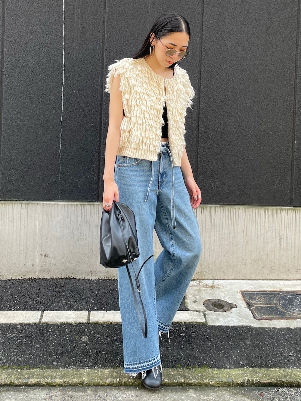 ブルー系のデニムパンツ、ホワイト系のベスト、ブラック系のショルダーバッグを着用したレディースの秋コーディネートの2枚目の写真