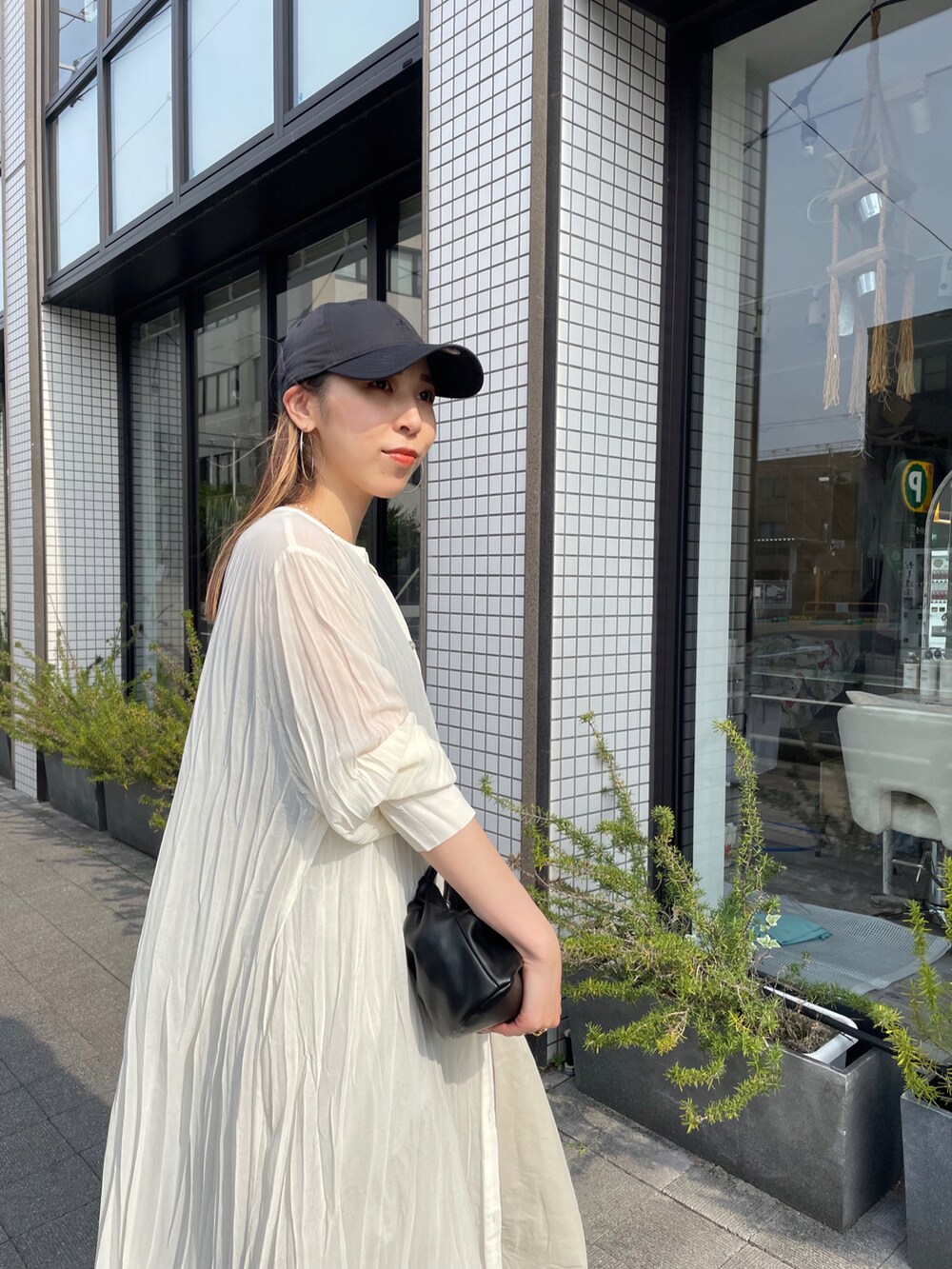 ブラック系のハンドバッグ、ホワイト系のワンピース、ブラック系のサンダルを着用したレディースの夏コーディネートの2枚目の写真