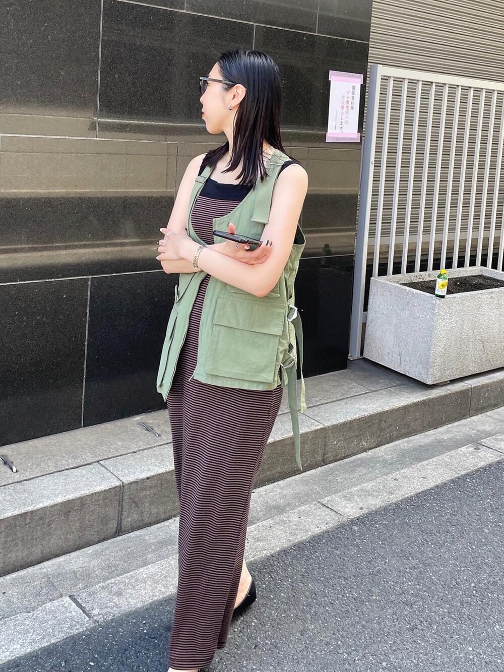 ブラック系のパンプス、ブラウン系のワンピース、グリーン系のベストを着用したレディースの春コーディネートの2枚目の写真