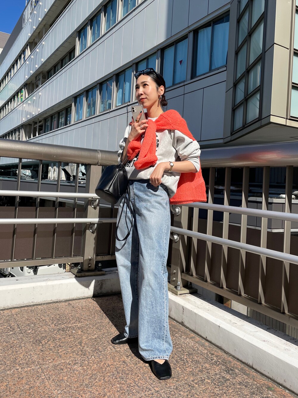 ブラック系のハンドバッグ、オレンジ系のニット/セーター、ブルー系のデニムパンツを着用したレディースの秋コーディネートの2枚目の写真